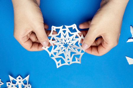 Hands holding white cutted paper snowflake on blue surfaceの写真素材