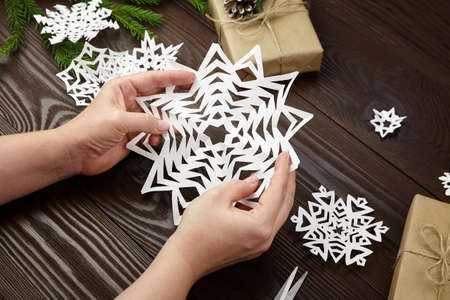 Hands holding white cutted paper snowflake over wooden tableの写真素材