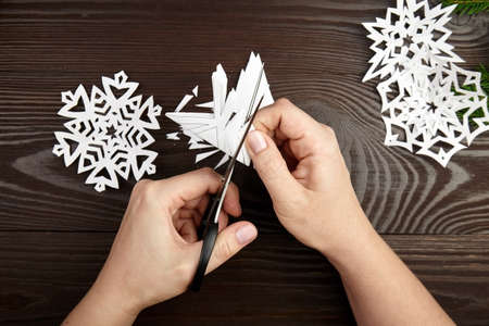 Hands cutting white paper snowflakes over wooden tableの写真素材