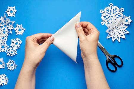 Hands making white paper snowflakes over blue backgroundの写真素材