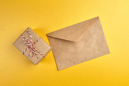 Craft paper envelope and gift box on golden background. Envelope for greeting card on yellow...