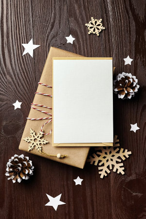 Christmas greeting card mockup with gift box, pine cones and wooden decorations on wooden background, flat lay, top viewの写真素材