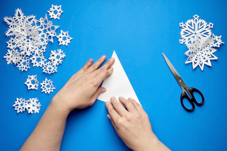 Hands making white paper snowflakes over blue backgroundの写真素材