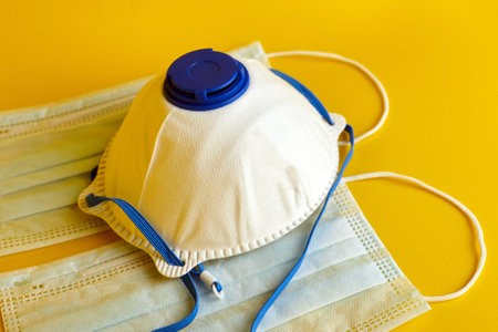 Respirator and surgical masks on yellow background. Disposable medical face masks. Airborne disease protection, COVID-2019, coronavirus pandemicの写真素材