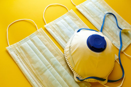 Respirator and surgical masks on yellow background. Disposable medical face masks. Airborne disease protection, COVID-2019, coronavirus pandemicの写真素材