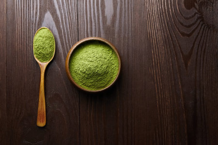 Wheatgrass or barley grass powder heap in wooden bowl and spoon on dark table background. Top view, copy space.の写真素材