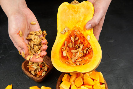 Woman removing pumpkin seeds and stringy fibers. Cooking sweet winter squash, fall resipe. Butternut squash, female hands with pumpkin half on black background, closeup, selective focusの写真素材