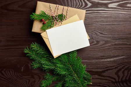 Christmas greeting card mockup with gift box and fir tree branches on brown wooden background, flat lay, top viewの写真素材