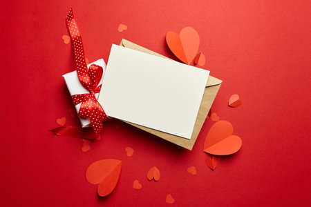 Blank greeting card or invitation. Valentines day card mockup with paper hearts and gift box on red backgroundの写真素材