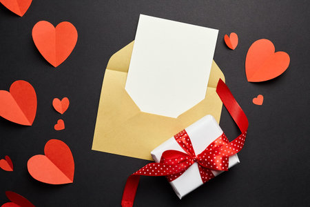 Greeting card mockup and gift box with paper decorations on black background. Blank greeting card or...
