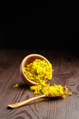 Hypericum perforatum or st johns wort plant flowers buds in bowl and spoon on dark wooden...