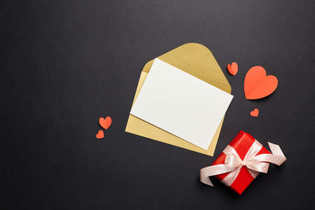 Greeting card mockup and gift box with paper decorations on black background. Blank greeting card or invitation, envelope and red paper heartsの写真素材
