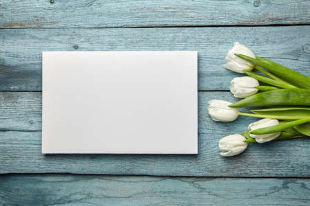 Canvas and white flowers on old light blue wooden background, flat lay. White blank canvas and tulips on table, mockup, front viewの写真素材