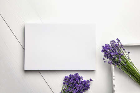 White canvas mockup and lavender flowers bouquet in tray on white wooden table background, flat lay. Blank canvas, top viewの写真素材