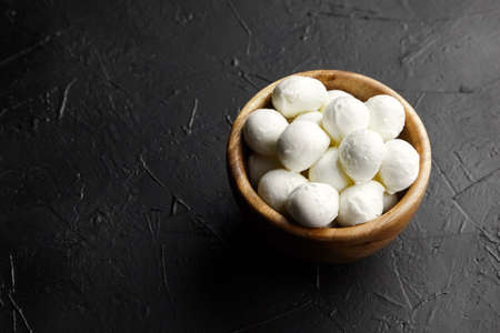 Wooden bowl with mini mozzarella cheese balls on black stony background, copy spaceの写真素材