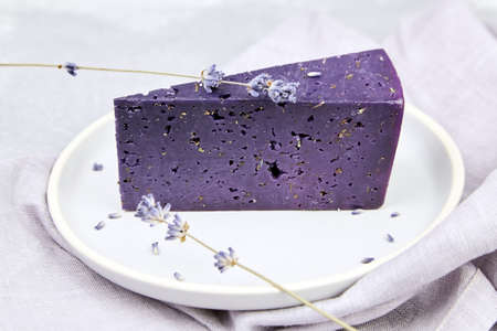 Lavender cheese with basil and lavender flowers in plate on concrete table with gray napkin. Piece of purple cheese with dry herbsの写真素材