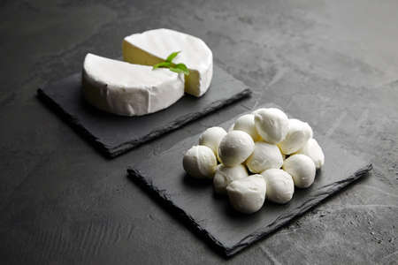 Mozzarella cheese balls and camembert cheese on black slate board over dark concrete backgroundの写真素材