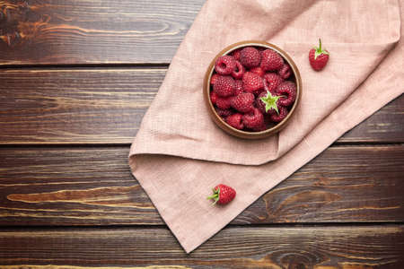 Fresh raspberries in wooden bowl on brown table with napkin, flat lay. Red ripe raspberries, sweet summer berries, top viewの写真素材