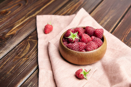 Fresh raspberries in wooden bowl on brown table with napkin. Red ripe raspberries, sweet summer...