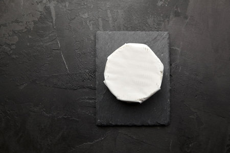 Camembert cheese head on black slate board over dark concrete background, italian food concept, copy space, top viewの写真素材