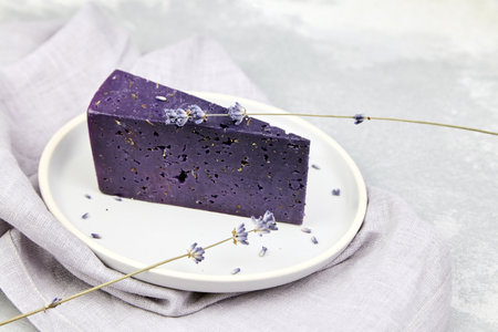 Piece of lavender cheese with dry basil and lavender flowers in plate on concrete table with gray napkinの写真素材