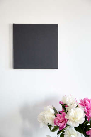 Black canvas mockup hanging on white wall and pink flowers. Blank artistic canvasの写真素材