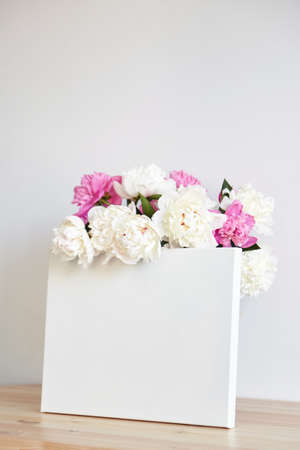 Canvas mockup with pink flowers on wooden table on white wall background. Blank artistic canvasの写真素材