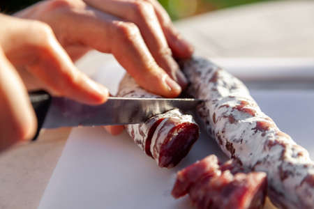 Men's hands cut with knife french cured sausage with white mold on cutting board closeupの写真素材