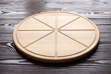 Round pizza cutting board with slice grooves on brown wooden tableの写真素材