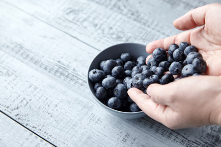 A handful of blueberries and bowl on wooden background closeupの写真素材