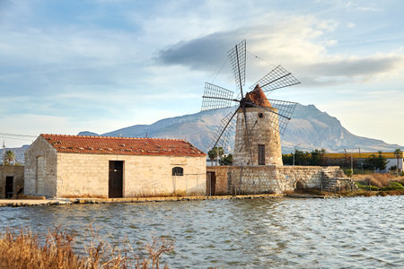 Windmill in Saline di Trapani e Paceco natural reserve near Trapani, Sicily, Italy. Pond and windmill overlooking town of Erice on mountainの写真素材