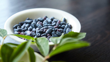 Fresh honeyberry (Lonicera caerulea) in white bowl on wooden table. Blue haskap berry with fresh...