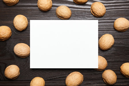 Blank card mockup with walnut shells on wooden background, top view, flat lay. White holiday card mock up on brown tableの写真素材