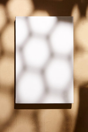 White canvas, blank picture mockup hanging on beige wall with dark shadows of geometric pattern....