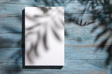 Canvas mockup, white blank picture hanging on blue wooden wall with dark shadows of palm leaves. Poster mock up, empty canvas with shadows of plant, front viewの写真素材