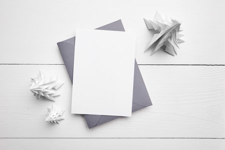 Holiday card mockup with envelope and white paper fir trees on white wooden background, top view, flat lay. Christmas greeting card mockup with decoration on tableの写真素材