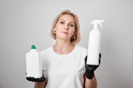 Woman holding cleanser in white bottles on grey background. Cleansing and disinfectant products. Caucasian woman holding detergent bottlesの写真素材