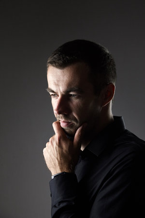 Portrait of pensive man in a black shirt on a dark background. Portrait of young caucasian dark-haired man. Novice businessmanの写真素材