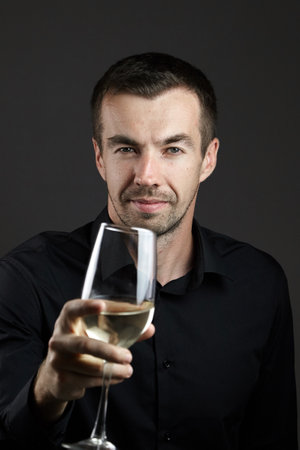 Portrait of smiling man in a black shirt with wine glass in hand on a dark background. Portrait of young caucasian dark-haired manの写真素材