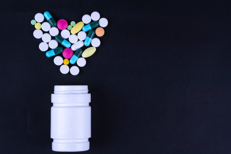 Assorted pharmaceutical medicine pills, tablets and capsules and bottle on black background. Copy...