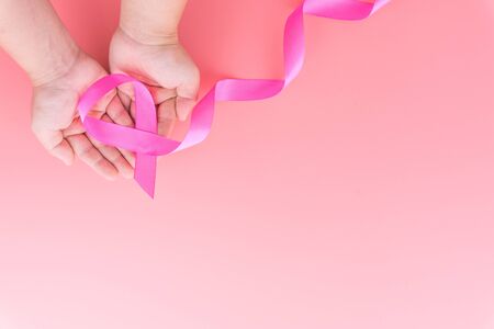 Woman hands holding pink ribbon breast cancer on pink background with copy space for text. Flat lay, top view.の写真素材