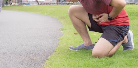 Sport man holding abdomen with his hands in stomach pain after running workout at park. Health care conceptの写真素材