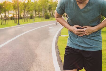 Sport man holding abdomen with his hands in stomach pain after running workout at park. Health care conceptの写真素材