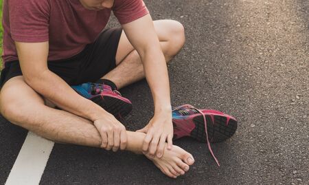 Ankle sprained. Young man suffering from an ankle injury while running at park. Healthcare and sport concept.の写真素材