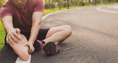 Young man massaging his painful foot from jogging and running on running track. Sport and exercise...