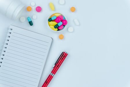 Assorted pharmaceutical medicine pills, tablets and capsules, pen and paper note on white background. Copy space for text, top view.の写真素材
