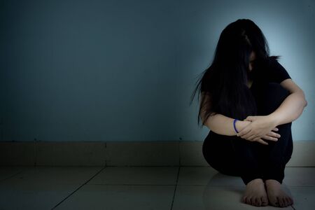 sad woman hug her knee and cry sitting alone in a dark room. Depression, unhappy, stressed and anxiety disorder conceptの写真素材