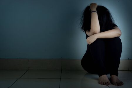 sad woman hug her knee and cry sitting alone in a dark room. Depression, unhappy, stressed and anxiety disorder conceptの写真素材