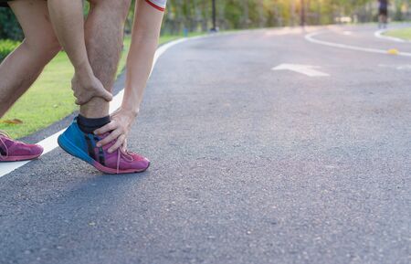 Ankle sprained. Young man suffering from an ankle injury while running at park. Healthcare and sport concept.の写真素材
