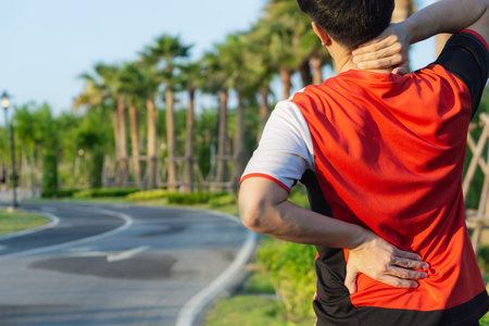 A male athlete suffering from neck and back pain and injury at the park. Sport and healthcare...
